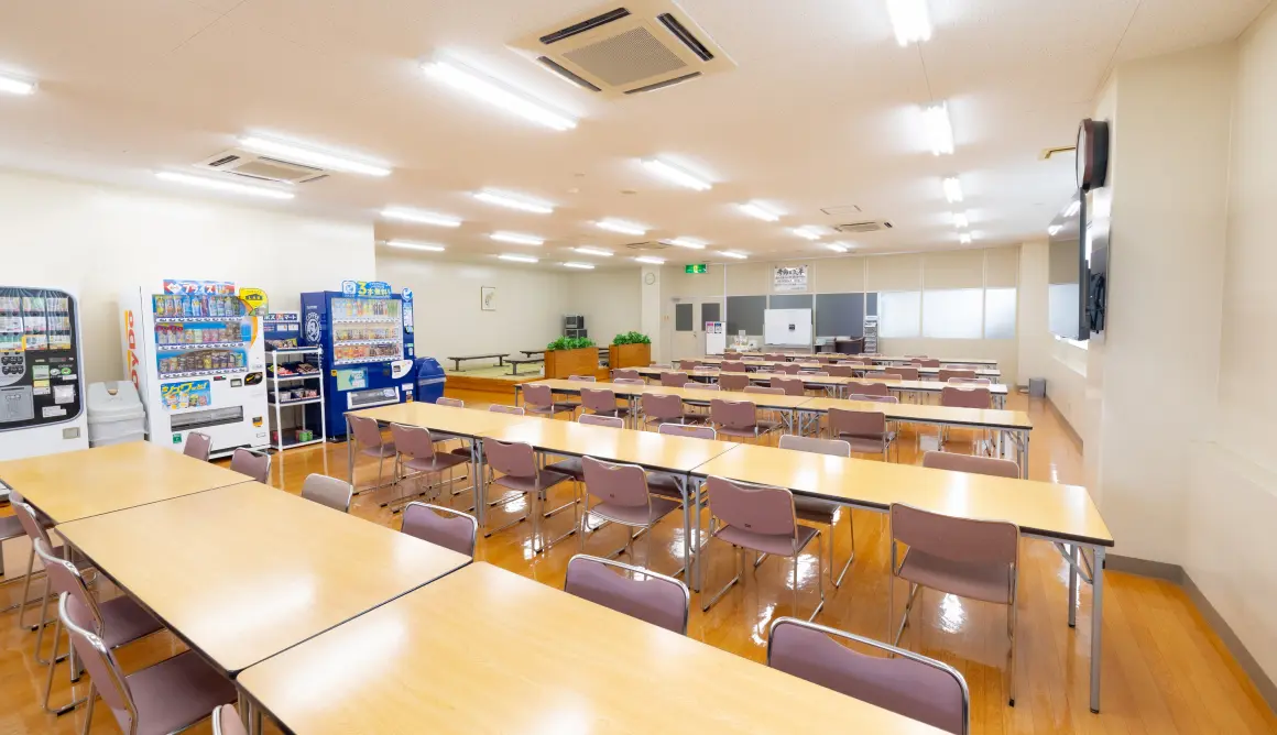 複数の自動販売機や複数の机や椅子が並んでいる部屋の写真